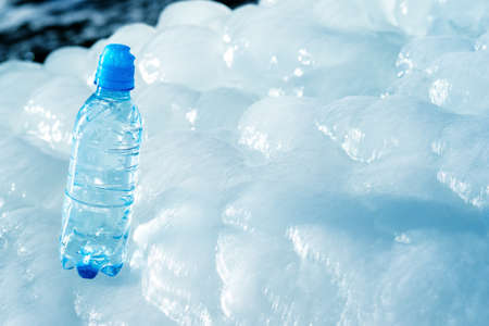Blue plastic bottle on ice against the background of the glacier meltwater flow. background. The concept of natural water purity.の写真素材