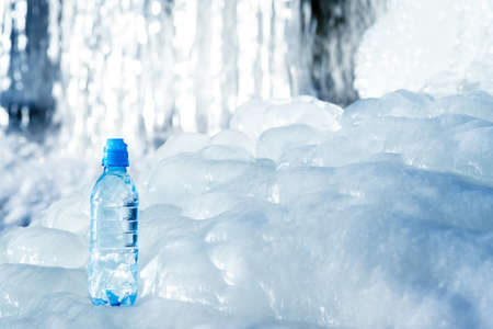 Blue plastic bottle on ice against the background of the glacier meltwater flow. background. The concept of natural water purity.の写真素材