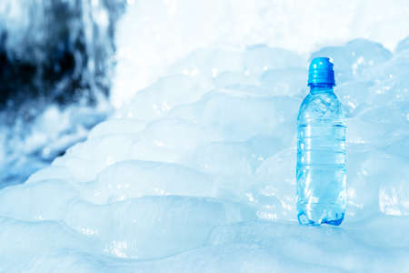 Blue plastic bottle on ice against the background of the glacier meltwater flow. background. The concept of natural water purity.の写真素材