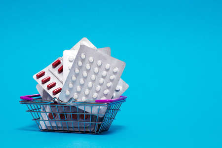 Heap of red and white pills and capsules are stacked in a metal basket on a blue background. The concept of various medicines and their properties, as well as medical dependence on medicines.の写真素材