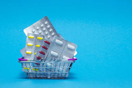 Heap of red, yellow and white pills and capsules are stacked in a metal basket on a blue background. The concept of various medicines and their properties, as well as medical dependence on medicines.の写真素材