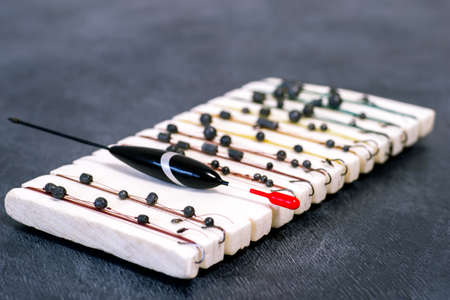 A black fishing float with a red antenna rests on a white reel with snap leads for different fishing...