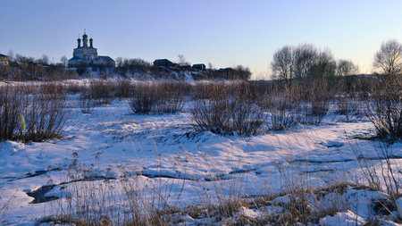 Landscape of a village with an old church in early spring on a frosty morning with the meltwater of a stream in the foreground. background.の写真素材