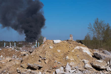 The concrete remains of a ruined building with protruding stilts against a background of black smoke against a blue sky. Backgroundの写真素材