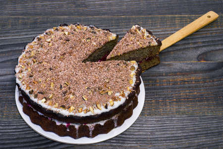 Chocolate cake decorated with grated chocolate with walnuts and a cut piece on a bamboo spatula with fruit filling on a wooden vintage background. The concept of making a cake.の写真素材