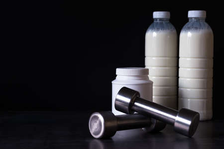 Dumbbells with protein powder and milkshake bottles in plastic packaging on a dark metal background. Background.の写真素材