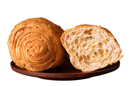 A bun with a golden crust and flax seed fractions for breakfast with yellow soy slices cut on a vintage clay plate, isolated on a white background.の写真素材