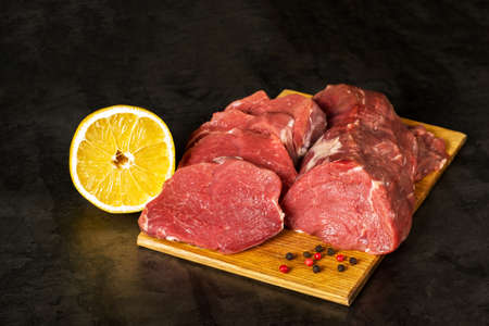 Fresh raw veal tenderloin meat in large chunks and sliced medallions on a wooden chopping board on a dark background.の写真素材