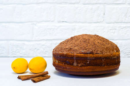 Lemon cake sprinkled with grated chocolate with lemons and cinnamon on a white table against a white decorated wall. The concept of making dessert.の写真素材