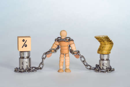 Figure of a man made of wood in chains tied to metal weights with the symbol of the dollar with coins and interest.の写真素材