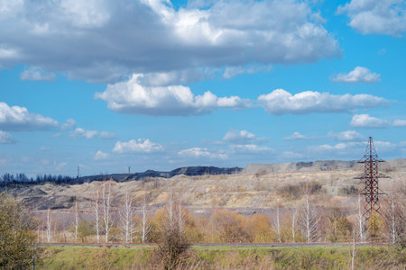 A deserted industrial landscape of rock dumps with remnants of forest, vegetation against the background of a spring sky with white clouds.の写真素材