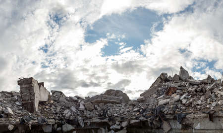 A pile of concrete gray debris of a destroyed building with a huge beam in the foreground against a blue sky with clouds. panorama.の写真素材
