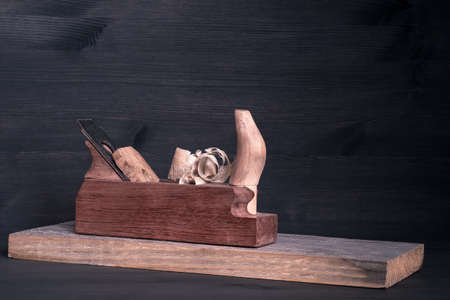 A wooden plane with protruding shaped shavings on a board on a dark background. background.の写真素材