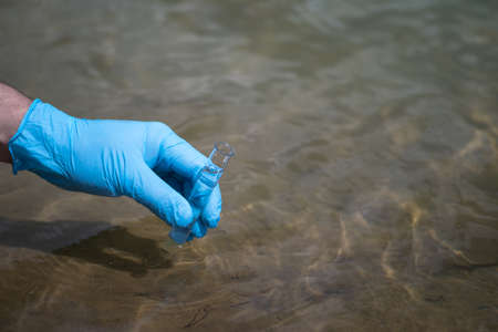 A mans hand in a blue glove takes a close-up of water into a test tube to measure the purity of water. Backgroundの写真素材