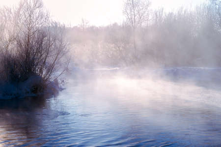 Winter landscape of the river in the morning haze with snow-covered banks and bushes covered with frost. background.の写真素材