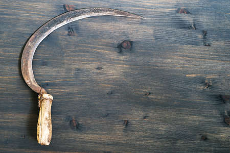 An old sickle on a wooden rustic dark background. top view.の写真素材