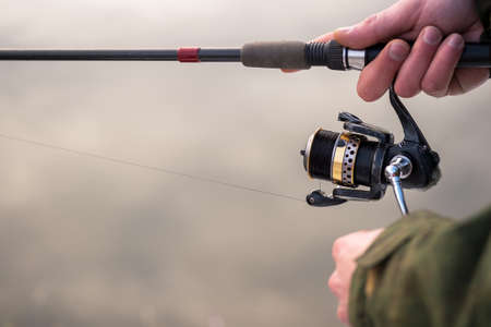 The frozen hands of a male angler close-up to hold the spinning motion wind the fishing line on a reel against the background of a winter river. Selective focus on the reel. background.の写真素材