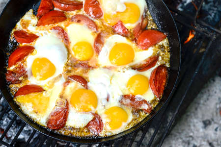 Scrambled eggs with tomatoes is prepared on a black pan on a metal lattice in the journey. The concept of the dish: a combination of protein and fiber. The view from the top.の写真素材