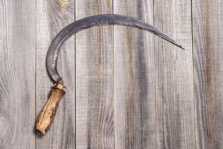 An old sickle on a wooden rustic plank gray background. Top view. Backgroundの写真素材