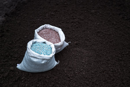 Two white bags with blue-white and brown pellets of industrial fertilizers on the background of a...