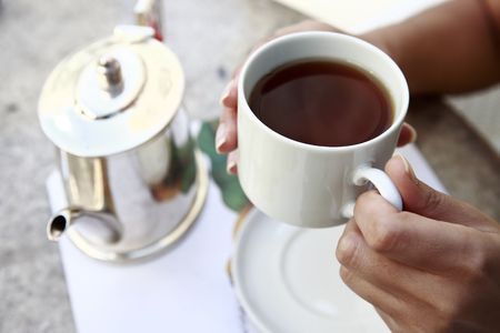 close up of hands serving tea in a cup from a teacup