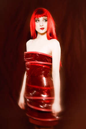 Funny & sexy expressive redhead girl wearing a palstic coat and dress on isolated backgrounの写真素材