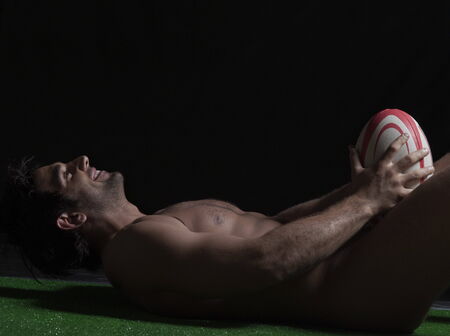 Naked young man lying with a rugby ballの写真素材