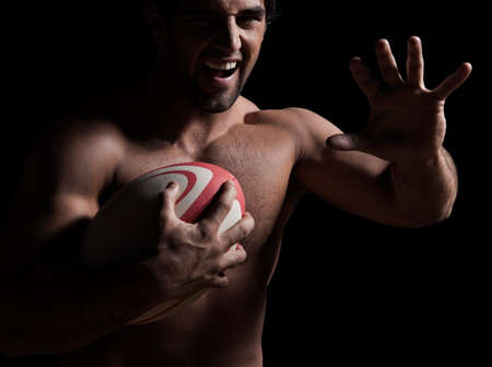 Portrait of a naked young man holding a rugby ball and laughingの写真素材