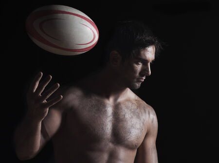 Close-up of a naked young man tossing a rugby ballの写真素材