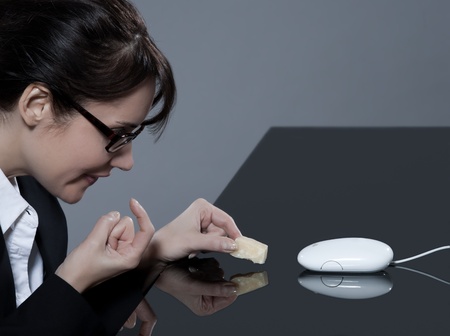 beautiful brunette business woman at her desk trying to trap her computer mouse with cheeseの写真素材