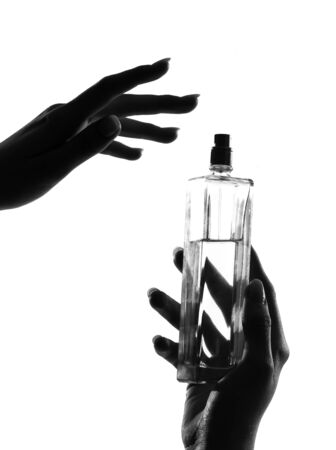 detail close-up silhouette in shadow of a  woman hands holding perfume in studio on white background isolatedの写真素材