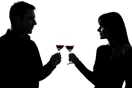 one caucasian couple man and woman drinking red wine toasting in studio silhouette isolated on white backgroundの写真素材