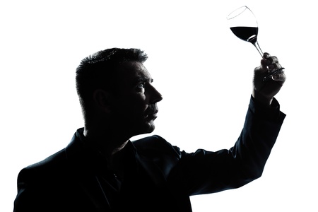 one caucasian man portrait silhouette tasting  looking at his glass of red wine in studio isolated...