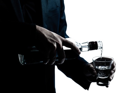 one caucasian man hands close up pouring white alcohol in a glass silhouette in studio isolated white backgroundの写真素材