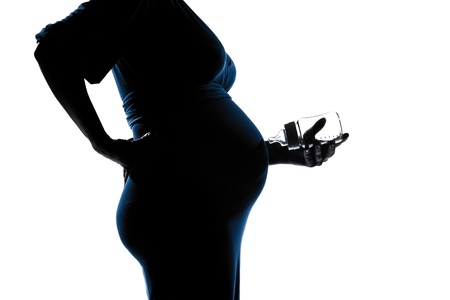 beautiful caucasian pregnant woman holding baby bottle in silhouette on studio isolated white backgroundの写真素材