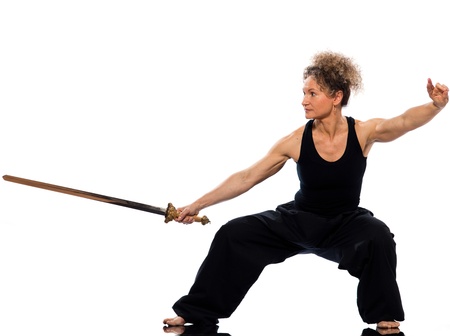mature woman praticing tai chi chuan with sword in studio on isolated white background