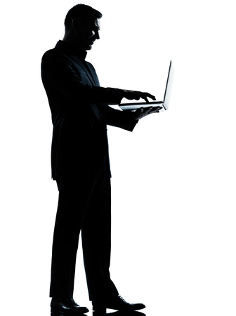 one caucasian business man computing computer laptop silhouette standing Full length in studio isolated on white backgroundの写真素材
