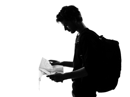 young man backpacker traveler looking at map silhouette in studio isolated on white backgroundの写真素材