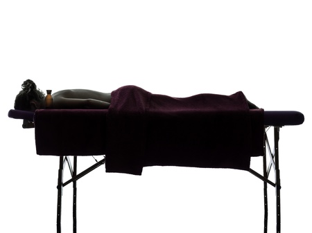 one woman lying on a massage table in silhouette studio on white backgroundの写真素材