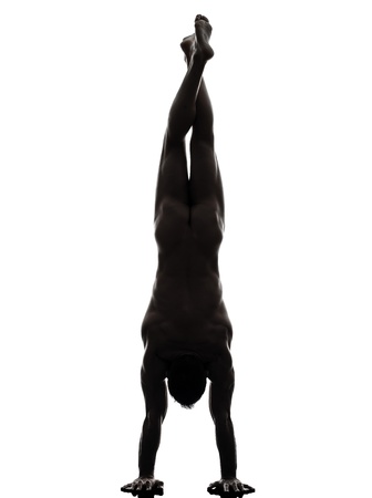one caucasian handsome naked muscular man exercising handstand in silhouette studio on white backgroundの写真素材