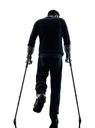 one  man injured man walking with crutches rear view  in silhouette studio  on white backgroundの写真素材