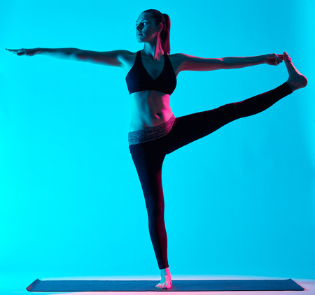 one caucasian woman exercising Hasta Padangusthasana yoga exercices  in silhouette studio isolated on blue backgroundの写真素材