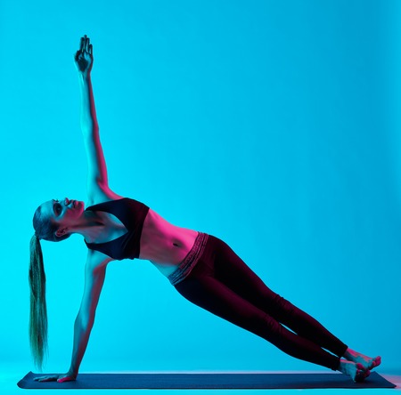 one caucasian woman exercising yoga exercices  in silhouette studio isolated on blue backgroundの写真素材
