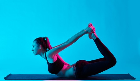 one caucasian woman exercising dhanurasana bow pose yoga exercices  in silhouette studio isolated on blue backgroundの写真素材