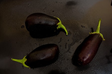 Three of eggplant in a chaotic manner above, with juicy drops of water on a black backgroundの写真素材
