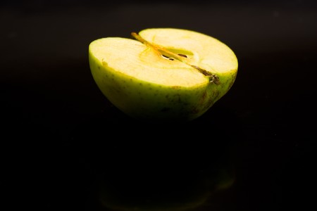 wet juicy green apple half on a black background with drops of juice is highlighted in brightの写真素材