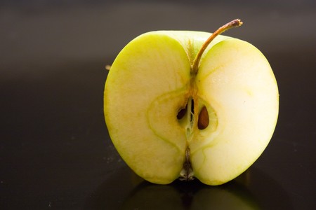 wet juicy green apple half on a black background with drops of juice is highlighted in brightの写真素材