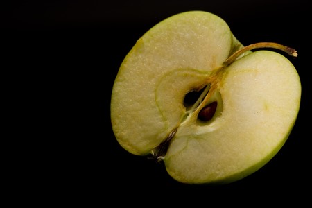 wet juicy green apple half on a black background with drops of juice is highlighted in brightの写真素材