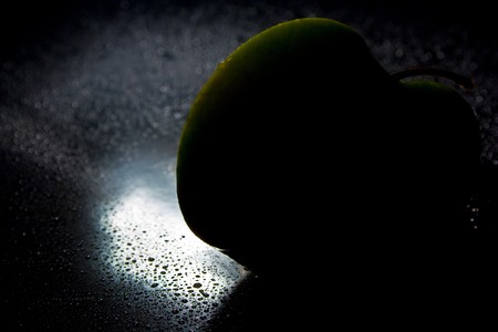 wet juicy green apple half on a black background with drops of juice is highlighted in brightの写真素材