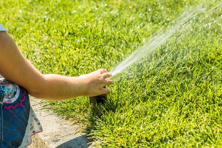 Little girl holding during irrigation, spray on the grassの写真素材